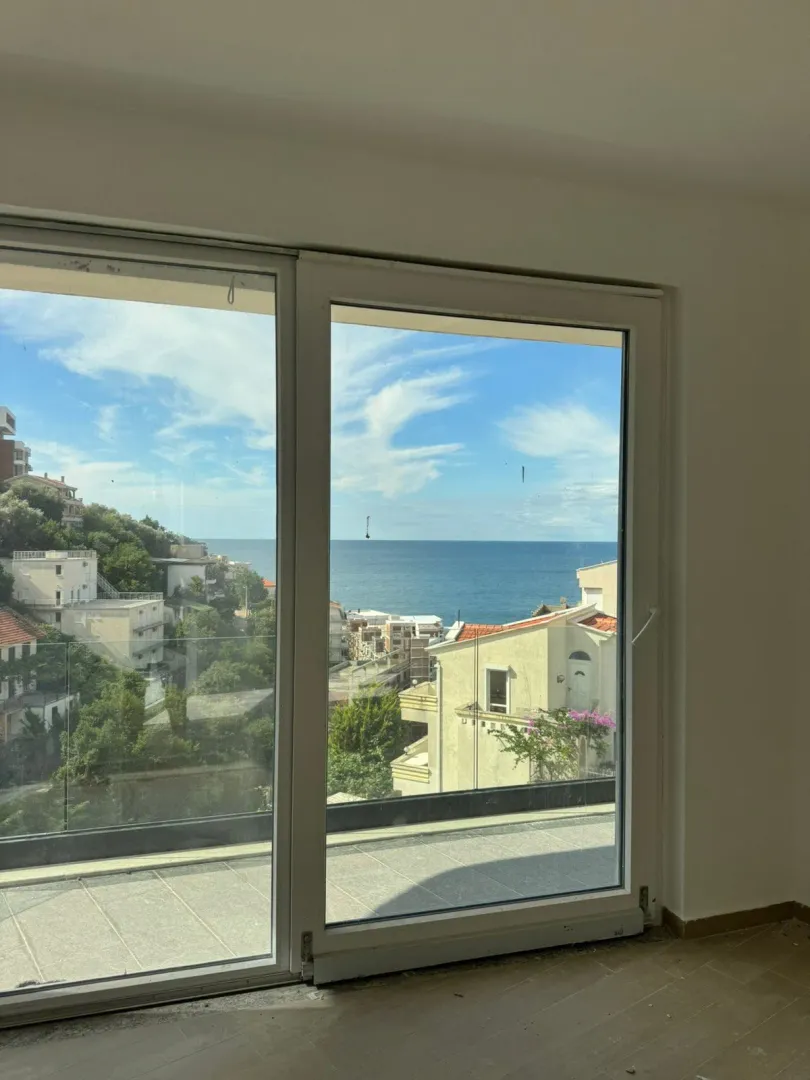 View of the sea and surrounding buildings through a large window.