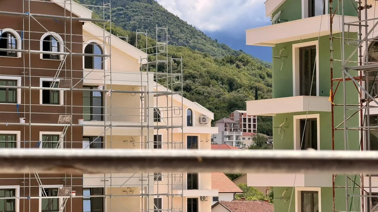 Pogled na zgrade u izgradnji sa skelama i brdima u pozadini.