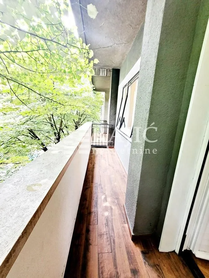 Long balcony space with wooden flooring and a view of trees.