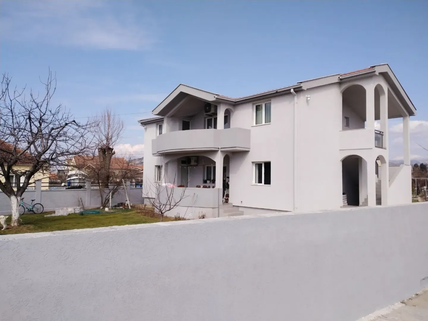 A two-story house with a fenced yard under a blue sky.