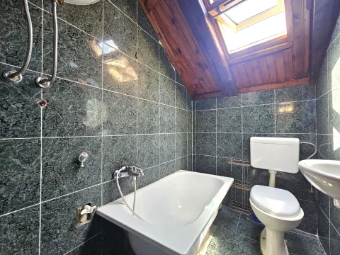 Small attic bathroom with a bathtub, toilet, sink, and a skylight window. - image 4