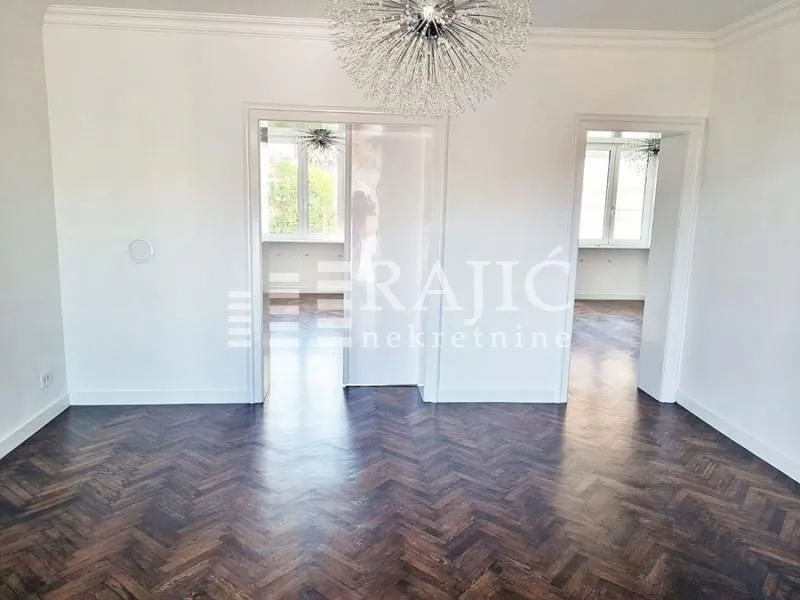 Spacious empty room with dark parquet flooring and white walls.