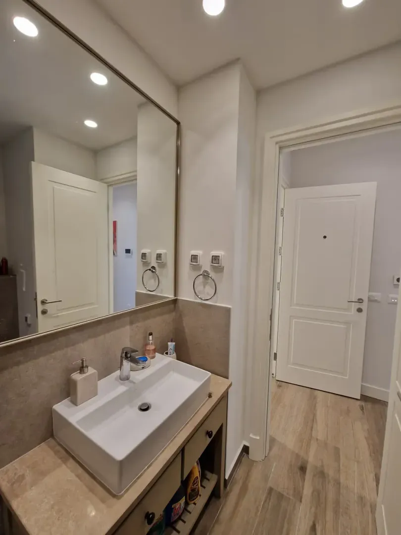 Modern bathroom with a washbasin, mirror and a door in the background.