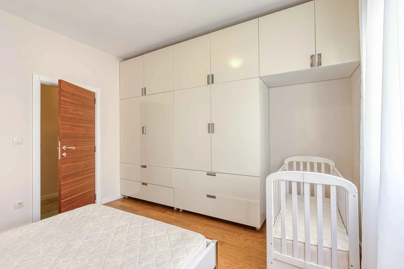Spavaća soba sa velikim ugradnim garderoberom i krevetićem za bebe.
