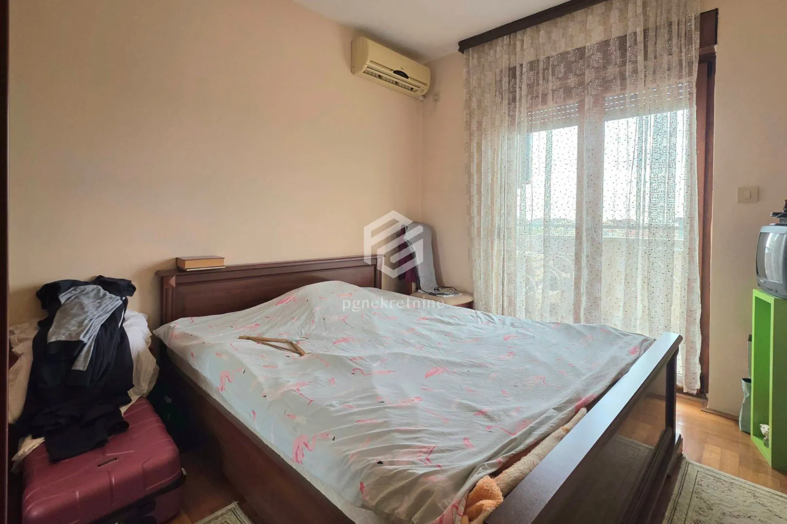 Namještena spavaća soba sa bračnim krevetom, klima uređajem i izlazom na balkon.