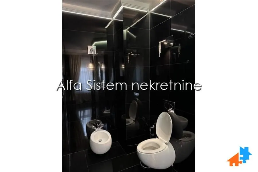 Moderno opremljeno kupatilo sa crnim pločicama i belom sanitarijom.