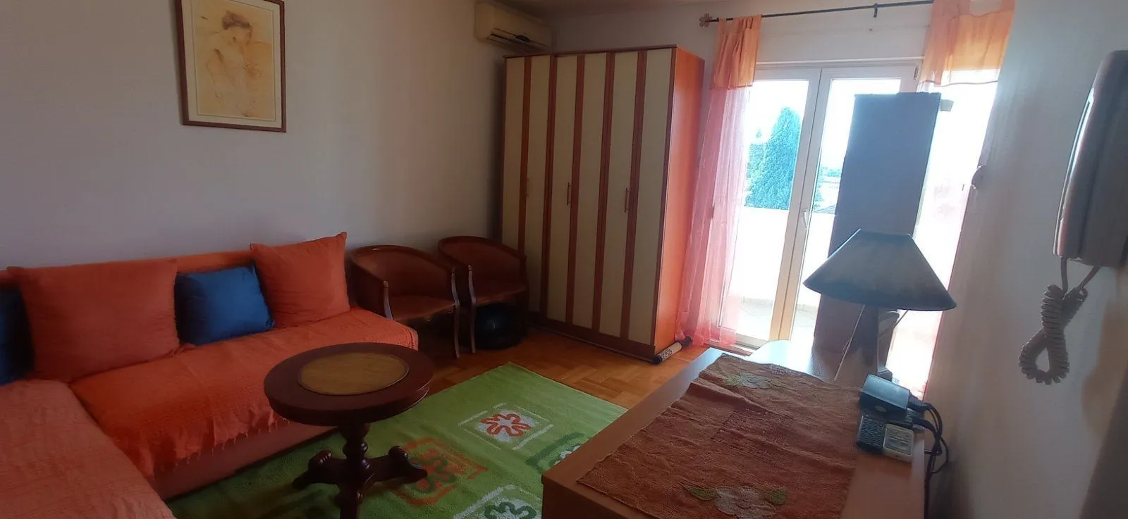 Living room with an orange sofa, wooden wardrobe, and balcony doors.