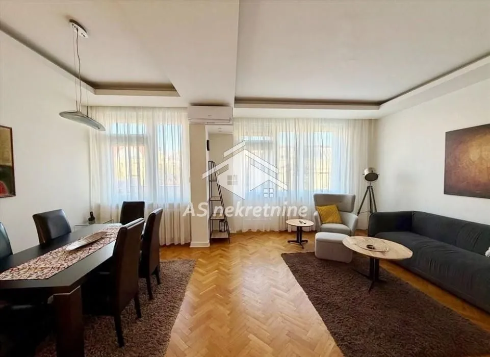 Spacious living room with sofa set, dining table and parquet flooring.