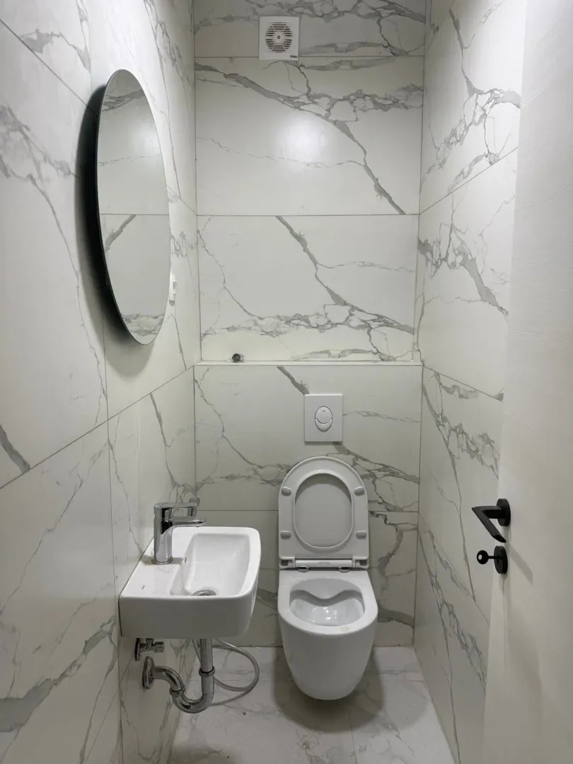 Small bathroom lined with marble-patterned ceramic tiles, featuring a basin and toilet.