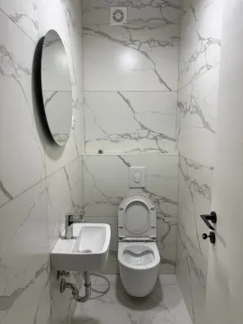 Small bathroom lined with marble-patterned ceramic tiles, featuring a basin and toilet. - image 4