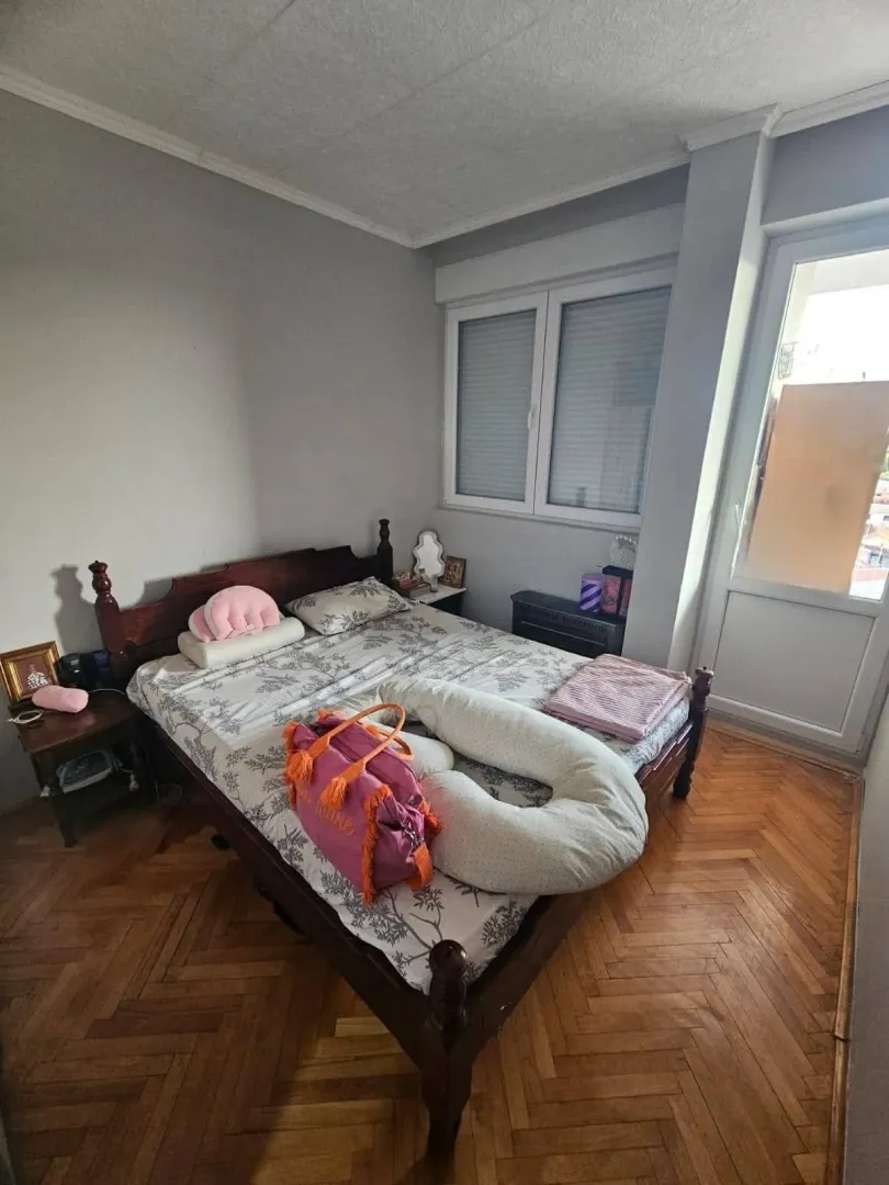 Spavaća soba sa bračnim krevetom, drvenim parketom i izlazom na terasu.