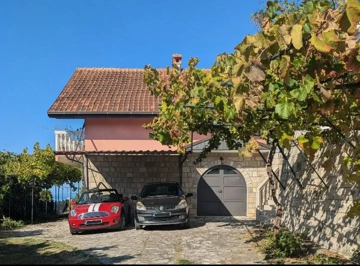Eksterijer kuće sa dvorištem, terasom i parkiranim automobilima.