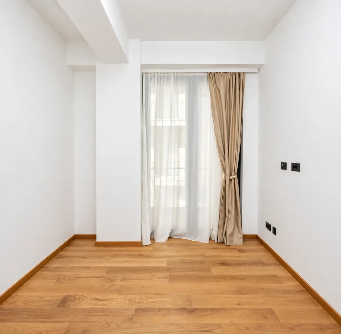 Empty bright room with wooden flooring and a window with curtains.
