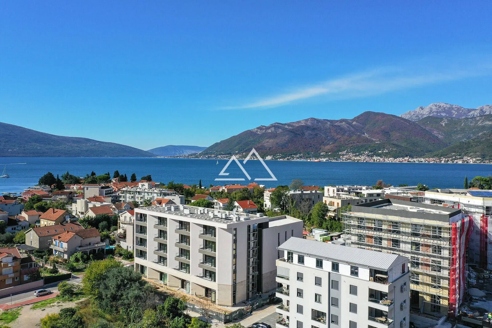 Pogled iz vazduha na stambene zgrade sa pogledom na more i planine.