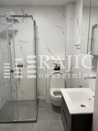 Modernly equipped bathroom with a shower cabin and marble tiles.