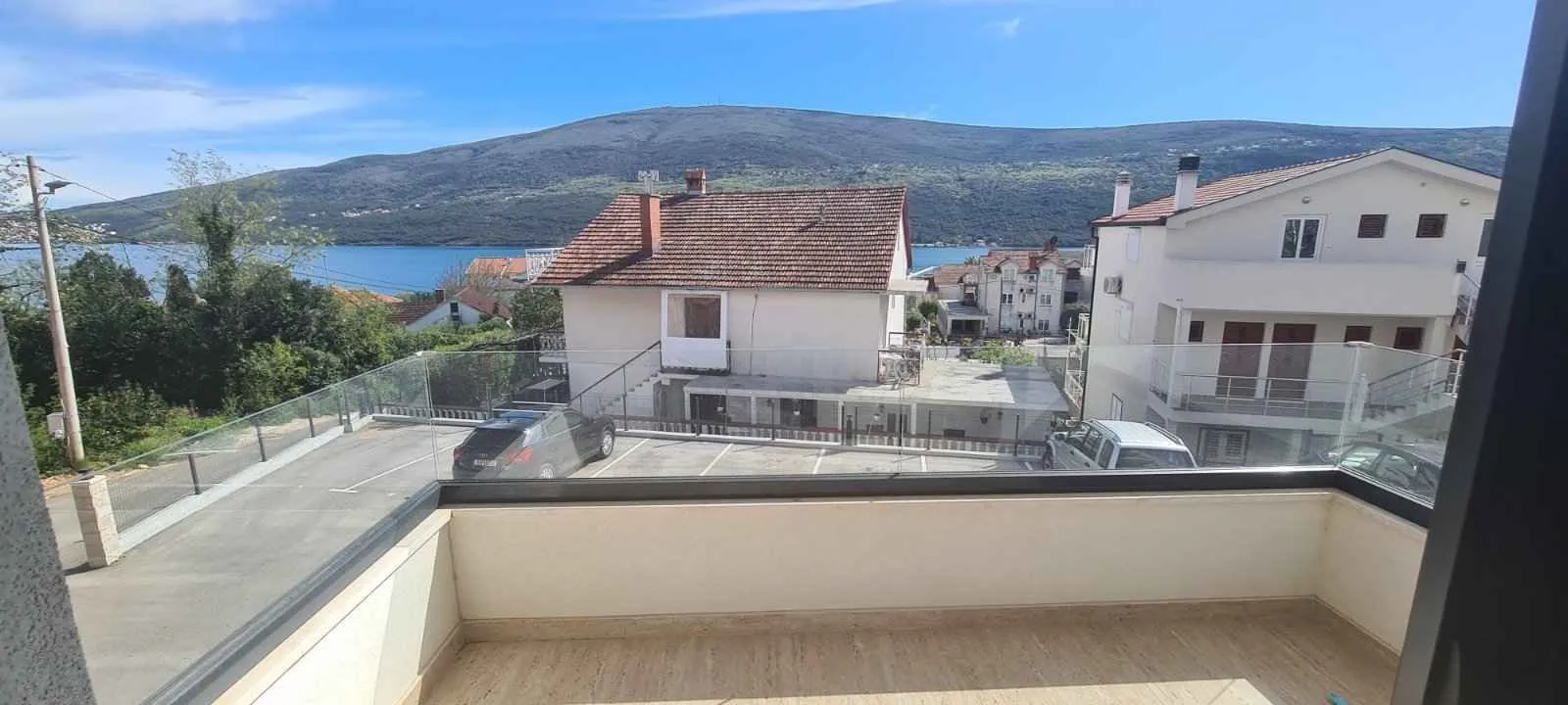 Pogled sa terase na okolne kuće, parking i planine u pozadini.