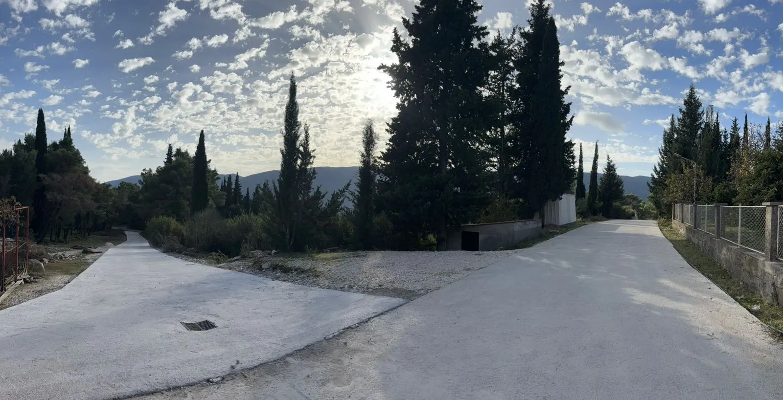 Asfaltirani prilazni put sa drvećem i rastinjem u okolini.