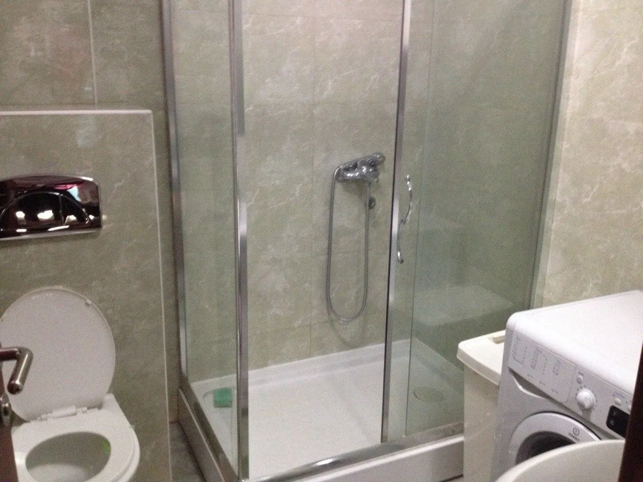 A bathroom featuring a glass shower cabin, a toilet, and a washing machine.