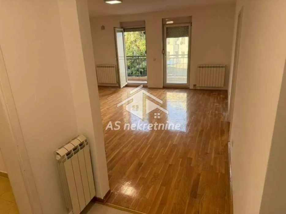 Prazna dnevna soba sa drvenim podom i izlazom na balkon.