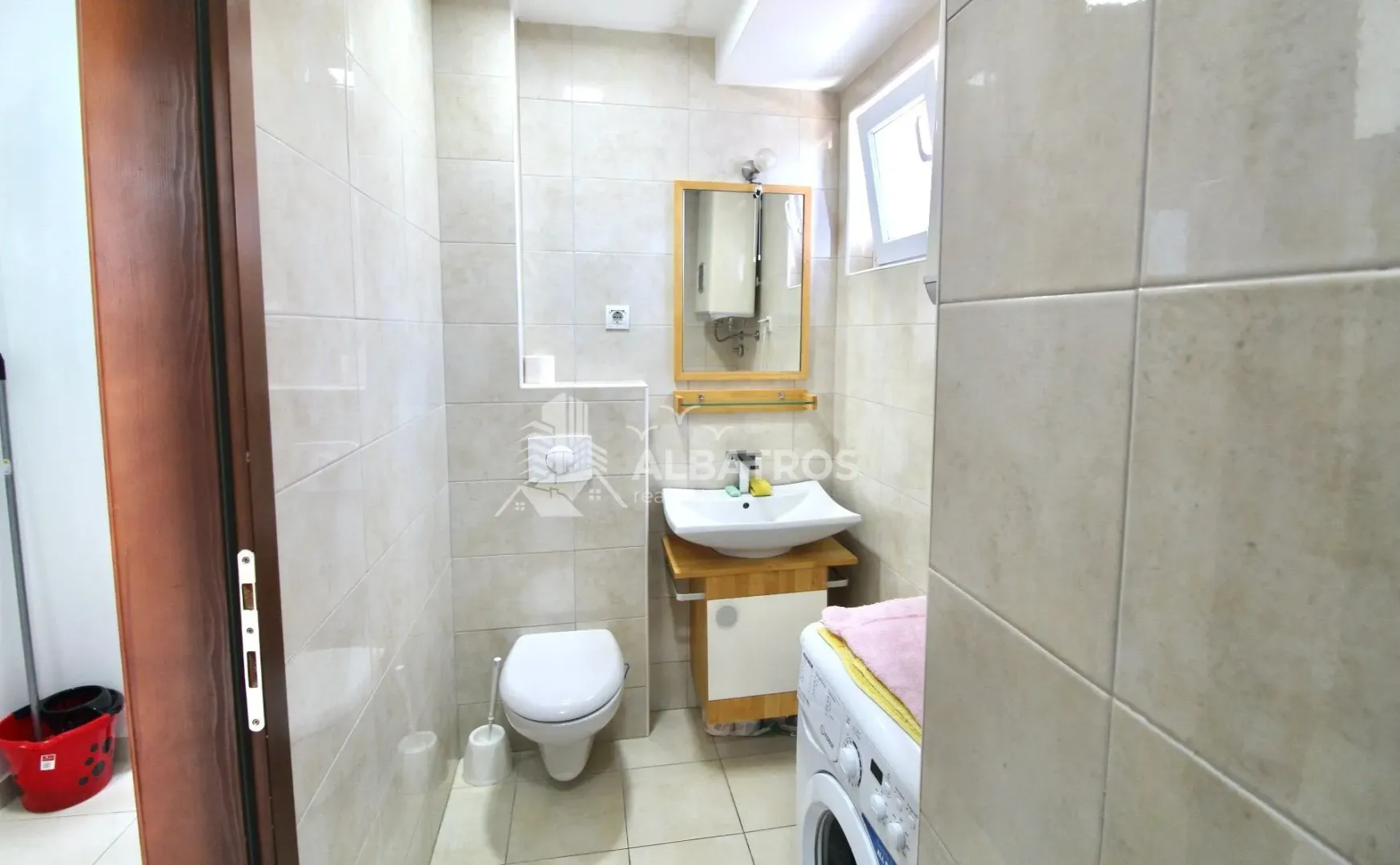 Small bathroom with a washbasin, toilet, mirror, and washing machine.