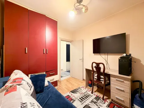 Manja spavaća soba sa krevetom, velikim crvenim garderoberom, radnim stolom i televizorom na zidu. - image 7