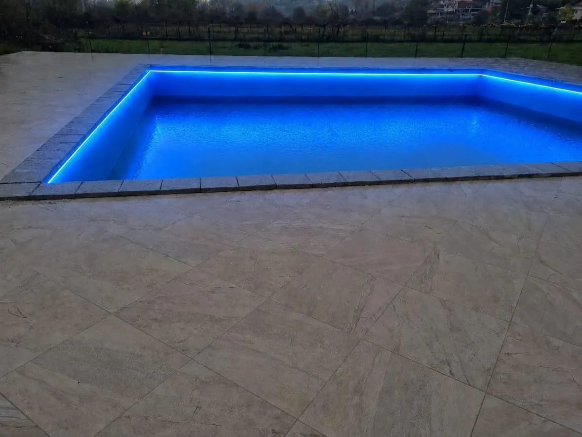 Swimming pool with blue LED lighting in a paved courtyard.