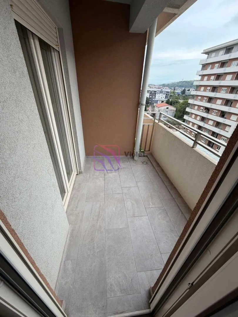 Nenamešten balkon sa pločicama i pogledom na grad.