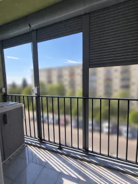 Zastakljeni balkon sa roletnama i pogledom na okolne zgrade i parking. - image 8