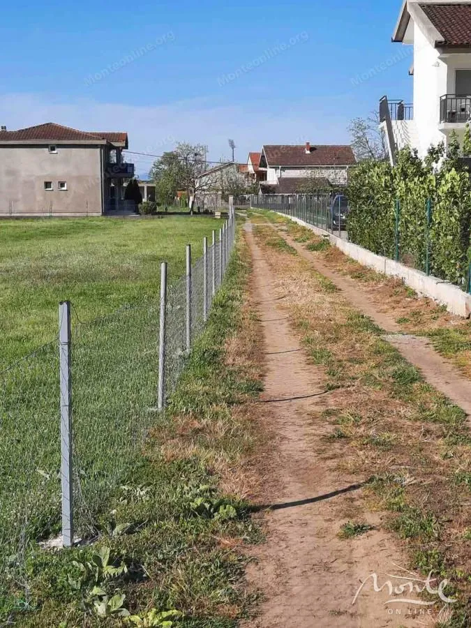 Zemljani put pored ograđenog placu u naselju sa kućama.