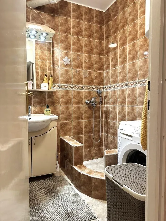 Bathroom tiled in brown with a walk-in shower, washbasin, and washing machine.