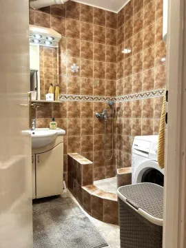 Bathroom tiled in brown with a walk-in shower, washbasin, and washing machine. - image 13