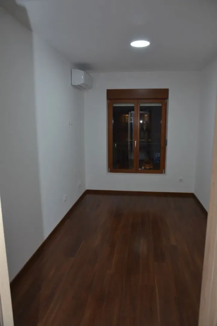 An empty room with dark flooring and a window.