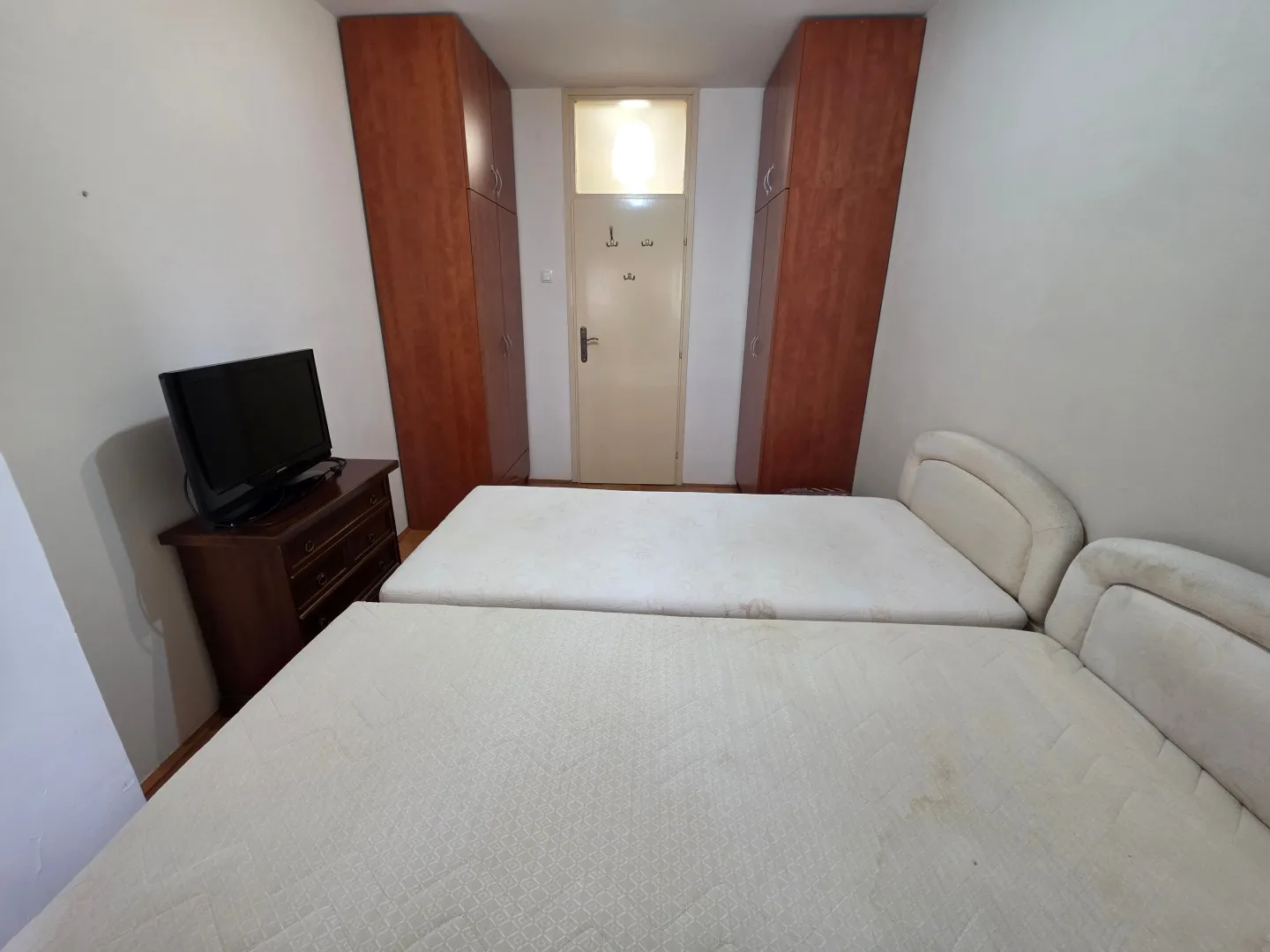 Furnished bedroom with two beds, wardrobes and a TV.