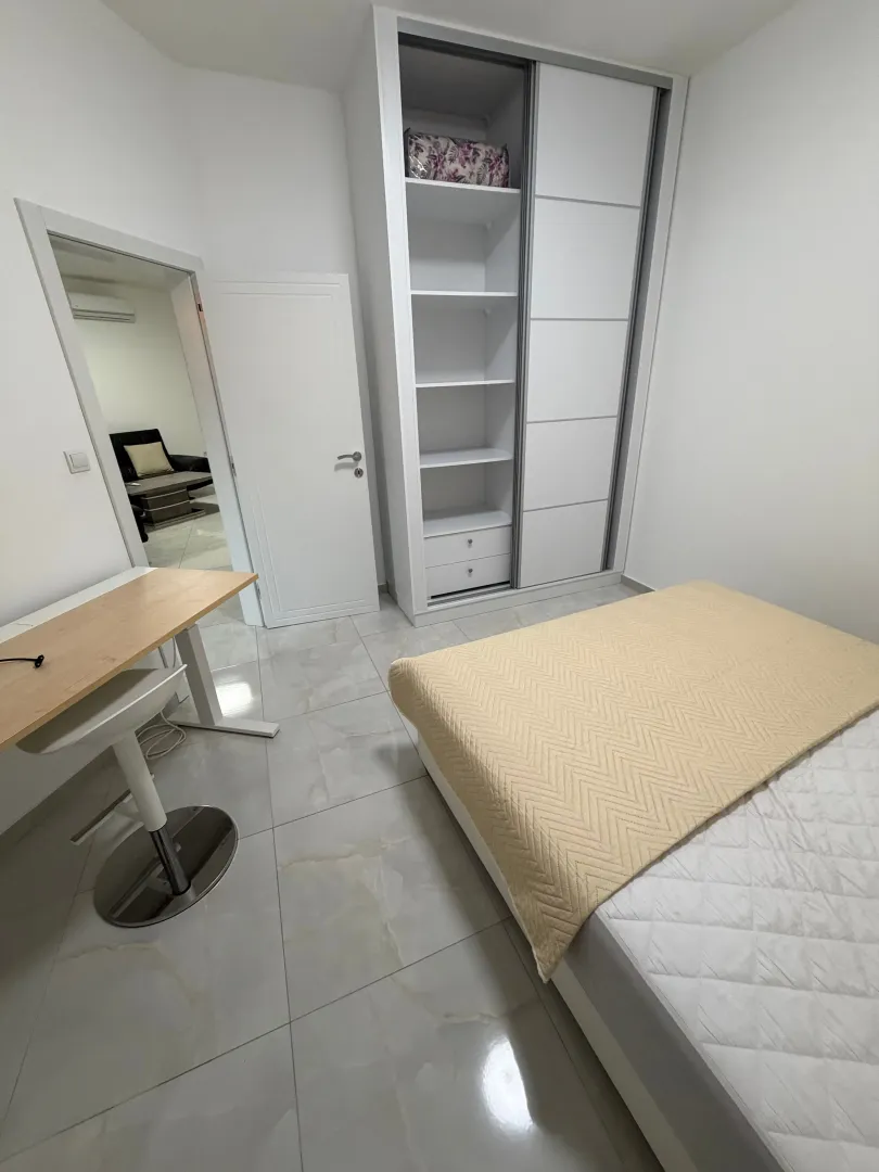 Bright bedroom with a bed, white wardrobe, and a desk.