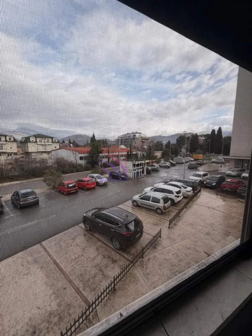 Pogled kroz prozor na parking i okolne zgrade.