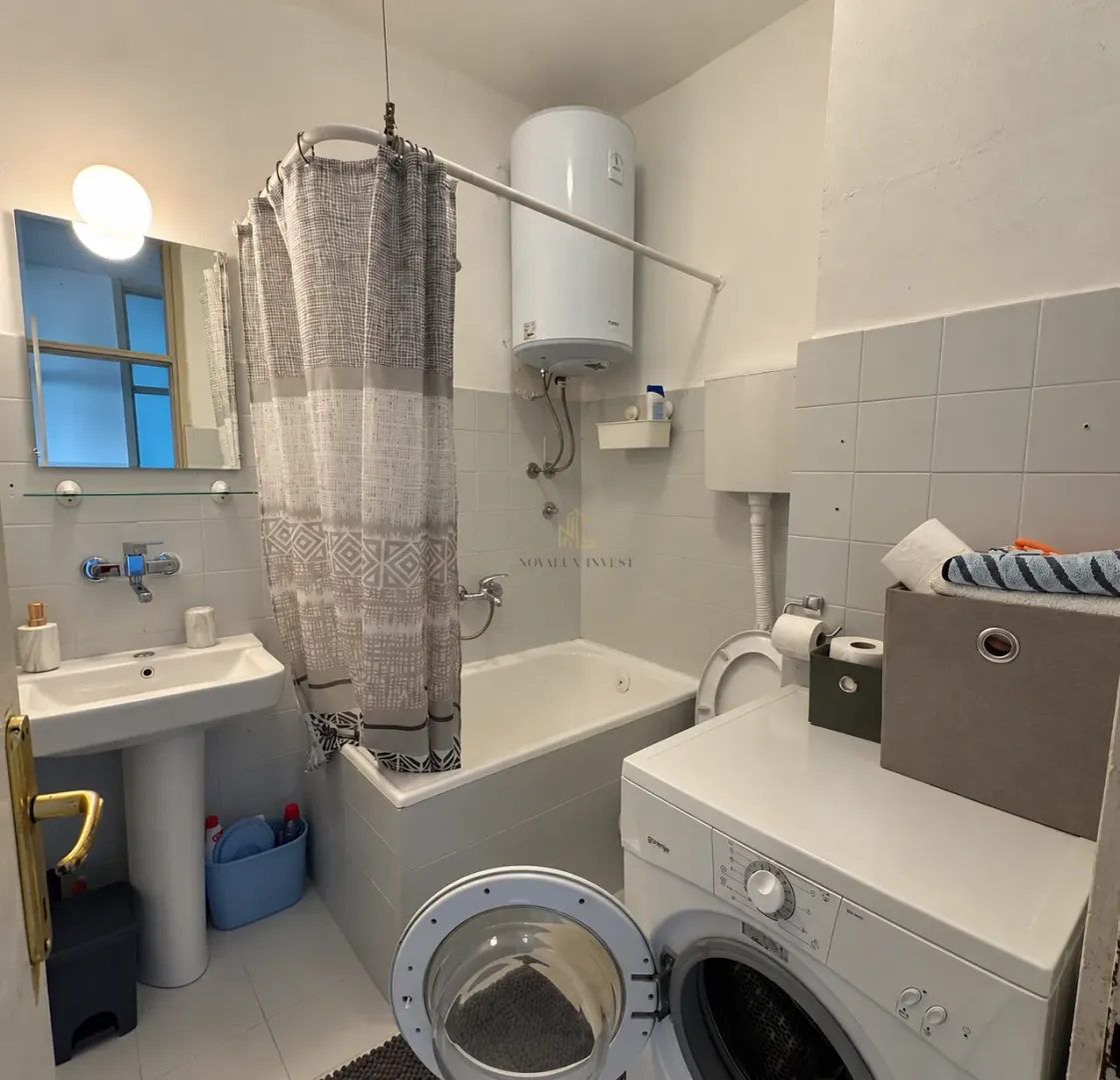 Manje kupatilo sa kadom, umivaonikom, WC šoljom i veš mašinom.