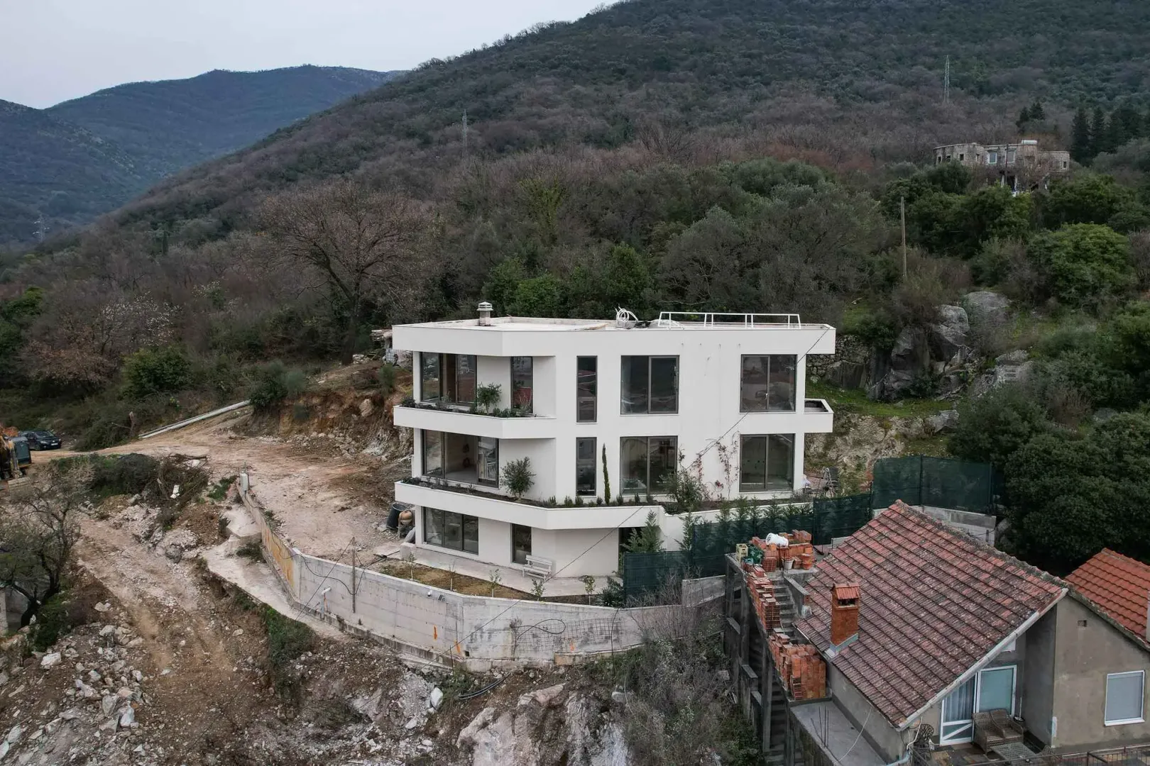 Pogled iz vazduha na modernu trospratnu kuću okruženu prirodom.