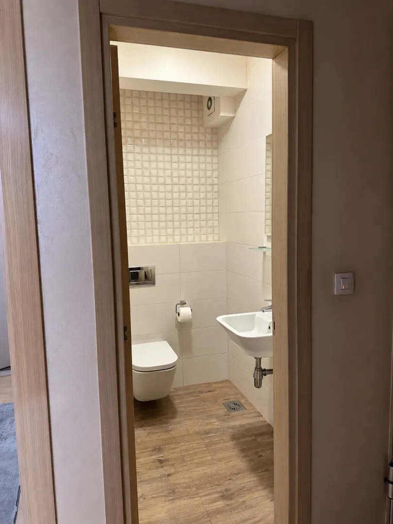 Pogled kroz vrata na moderno opremljeno kupatilo sa WC šoljom i umivaonikom.