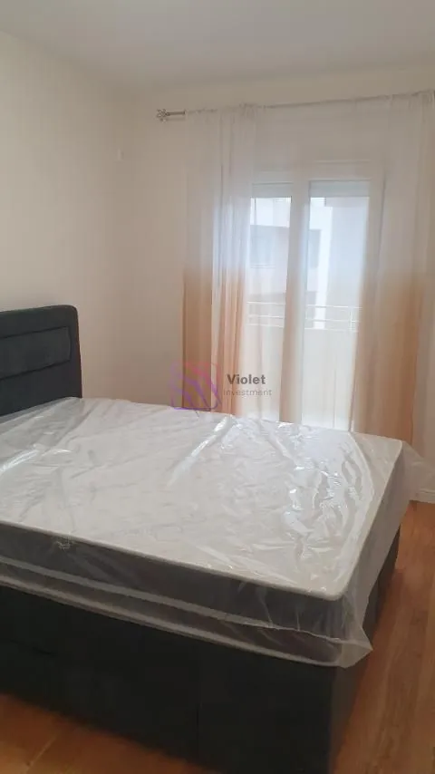 Namještena spavaća soba sa bračnim krevetom i prozorom sa zavjesama.