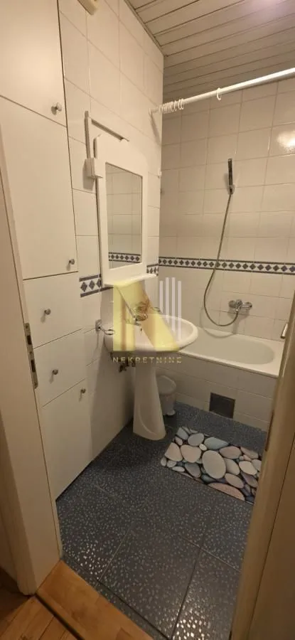 Kupatilo sa kadom, umivaonikom i belim ugradnim ormarićem.