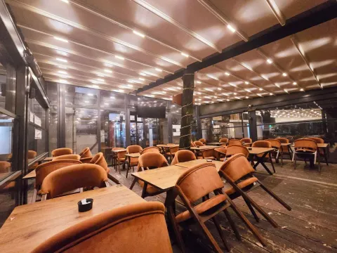 Covered terrace with wooden tables and upholstered chairs. - image 4