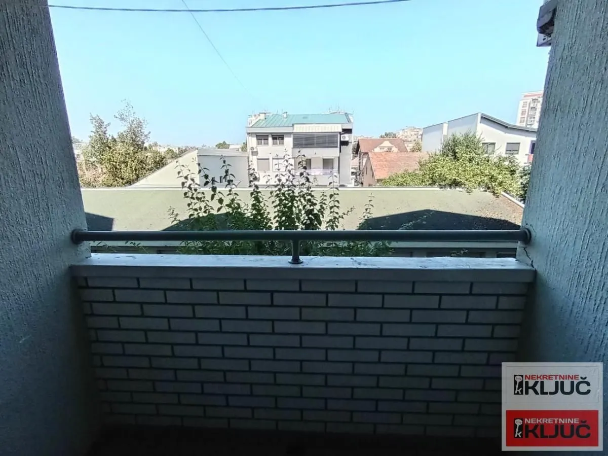 Pogled sa balkona na okolne zgrade i zelenilo.