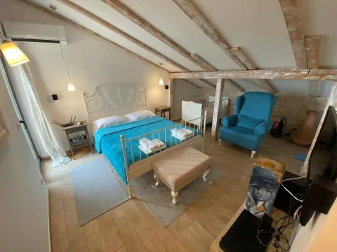 Attic bedroom with a bed, blue armchair, and wooden ceiling beams. - image 5