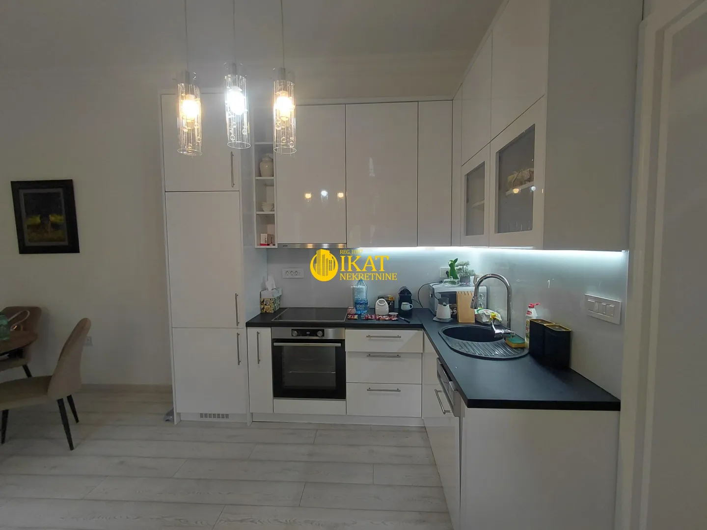 Modern white kitchen with black countertops and built-in appliances.