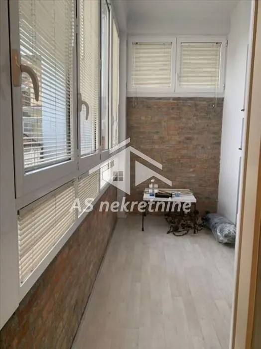 Zastakljena terasa sa velikim prozorima i zidom obloženim ciglom.