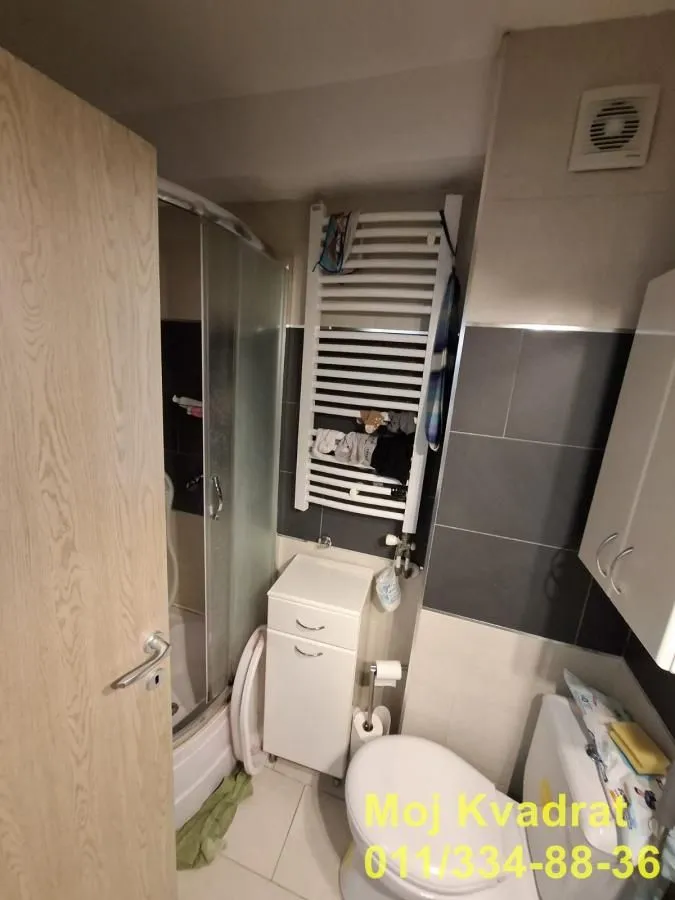 Manje kupatilo sa tuš kabinom, WC šoljom i belim ormarićem.