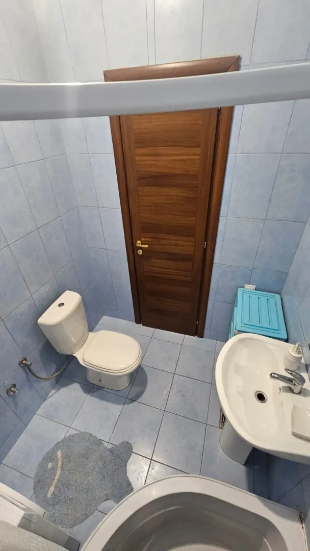 Manje kupatilo sa plavim pločicama, umivaonikom i toaletom.