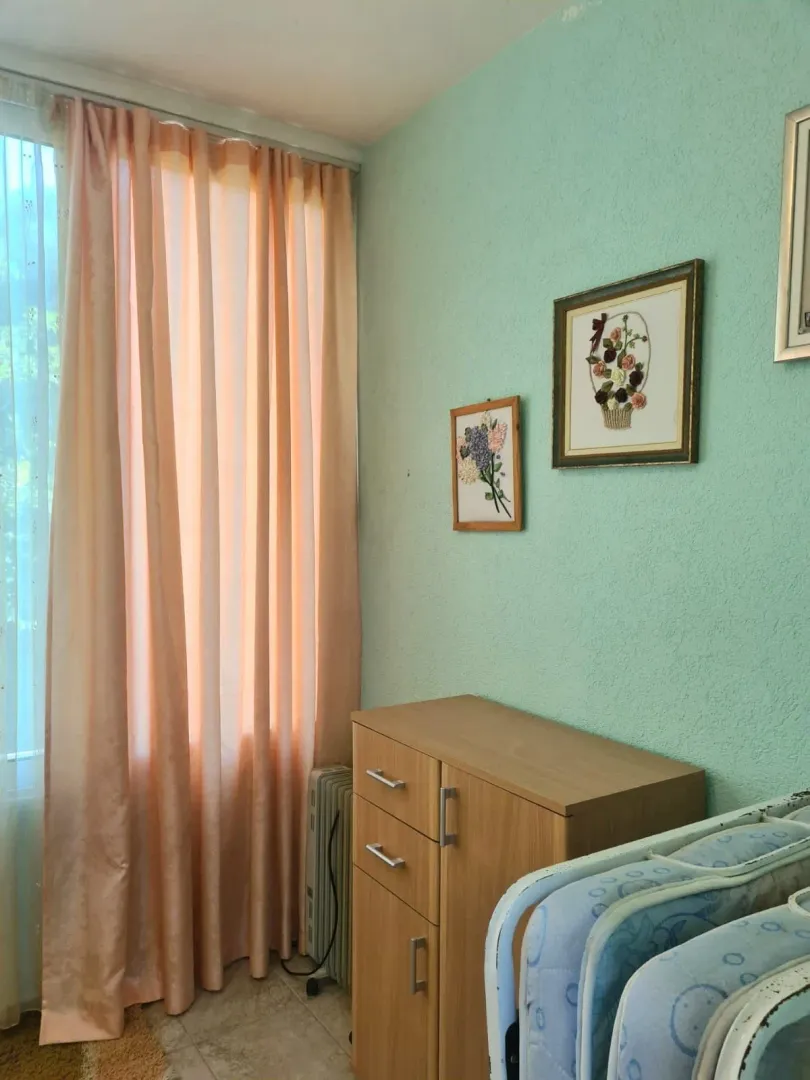 Pogled na dio spavaće sobe sa krevetom, komodom i prozorom sa zavjesama.
