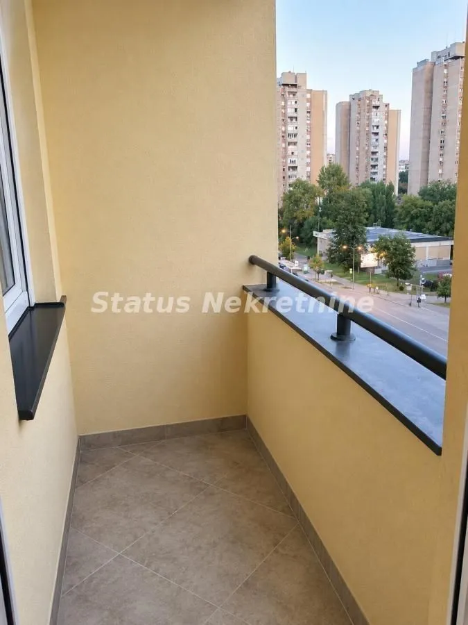 Small tiled balcony with a black railing and a city view.