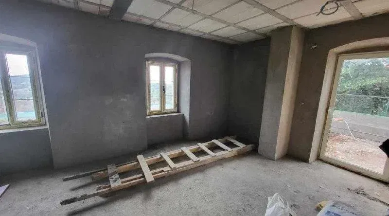 Nepotpun prostor u izgradnji sa sivim zidovima, prozorima i vratima koja vode na terasu.